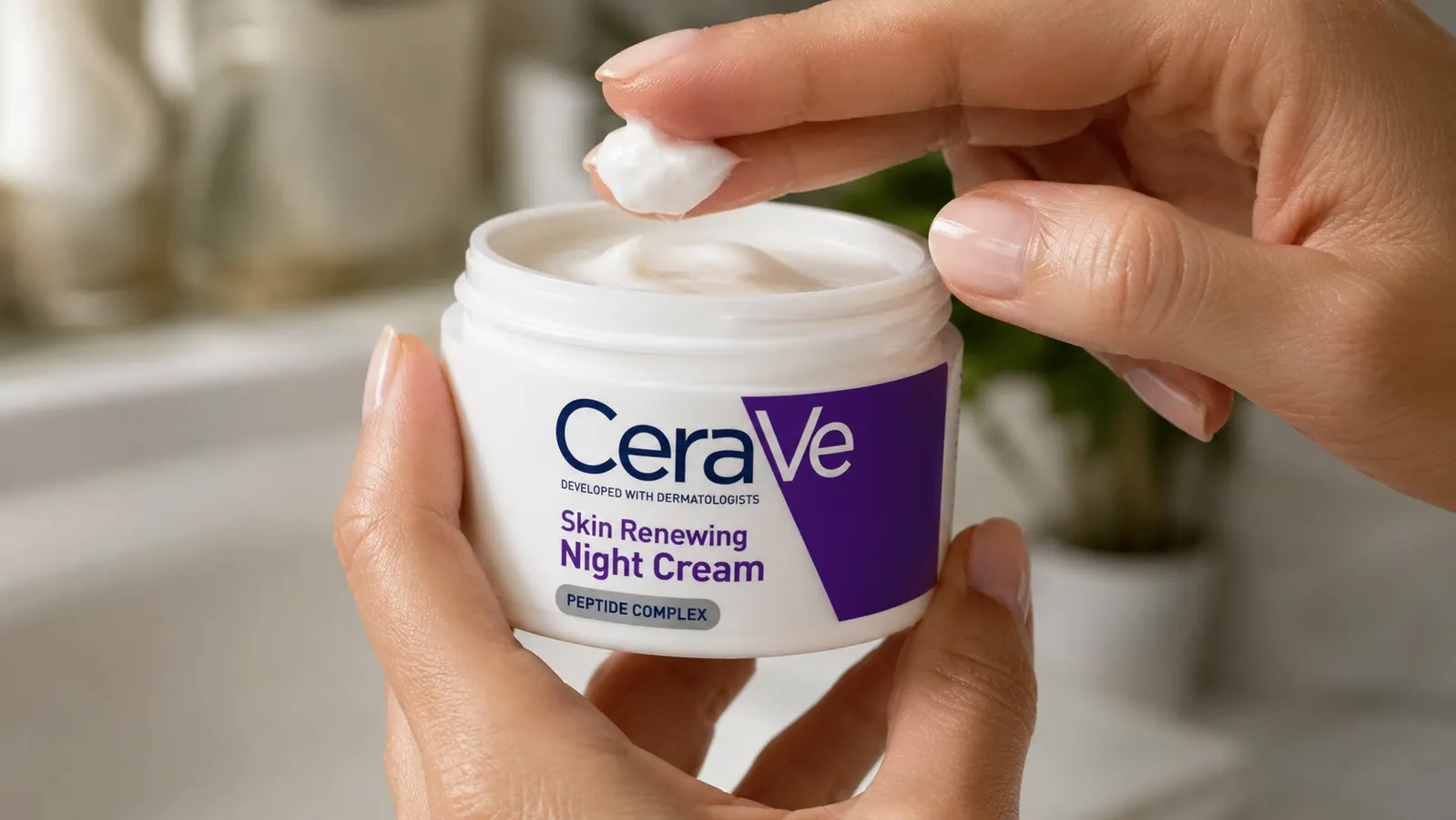 A hand scooping a small amount of thick white night cream from an open jar