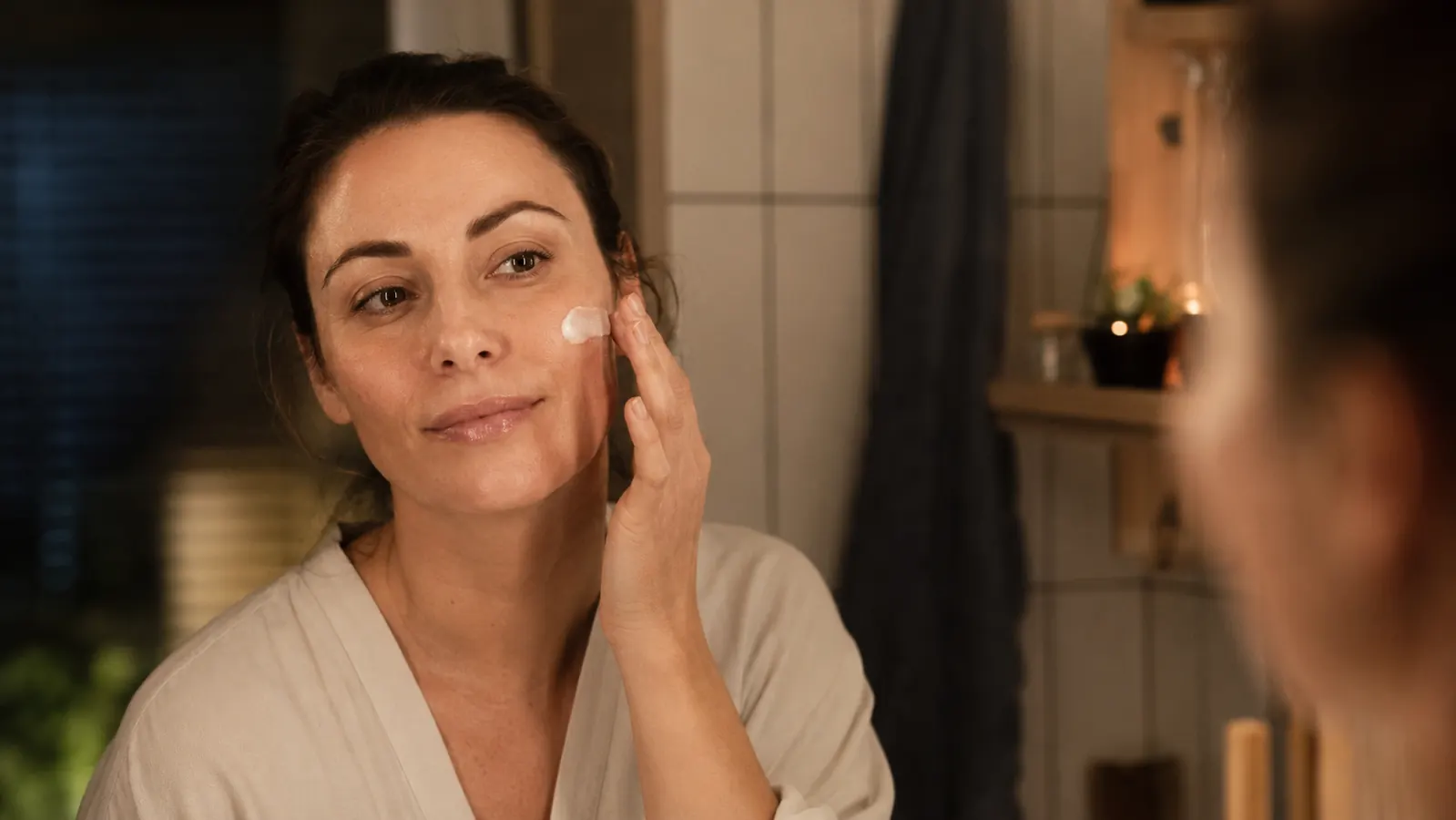 Close-up of a woman applying moisturizer to her cheek before bed
