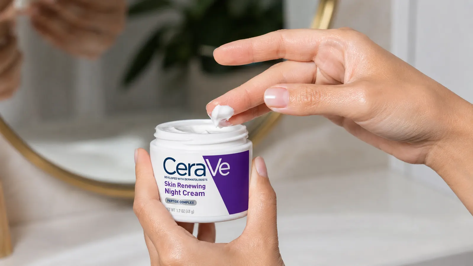 Hand scooping a small amount of CeraVe night cream from the jar before applying to skin