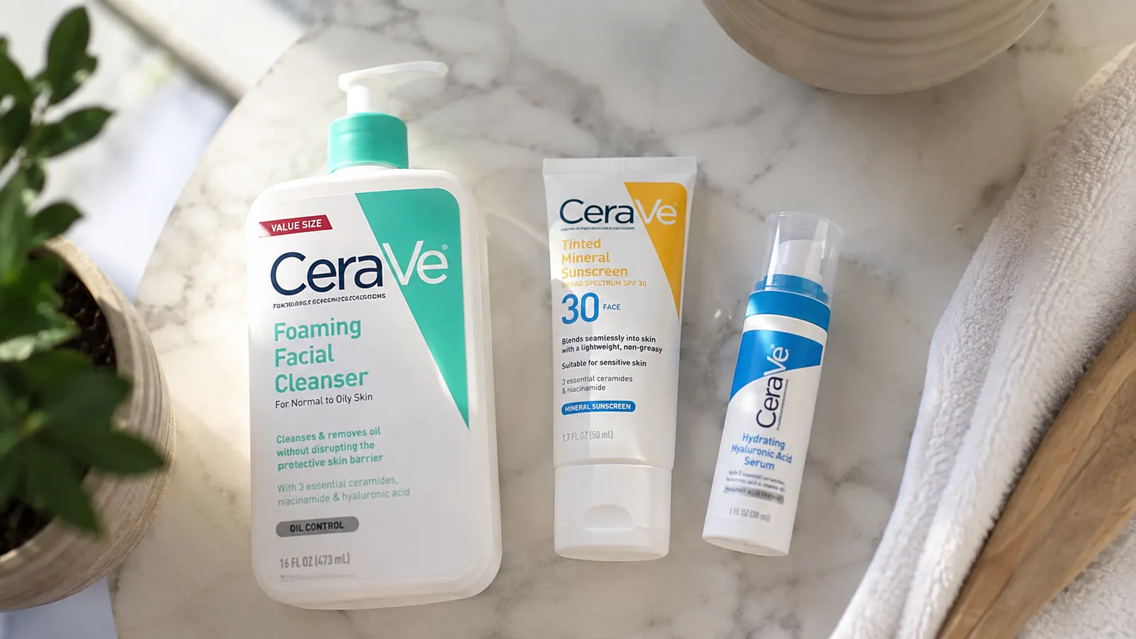 Closeup of product pump tube next to a daily skincare routine flat lay on a marble surface