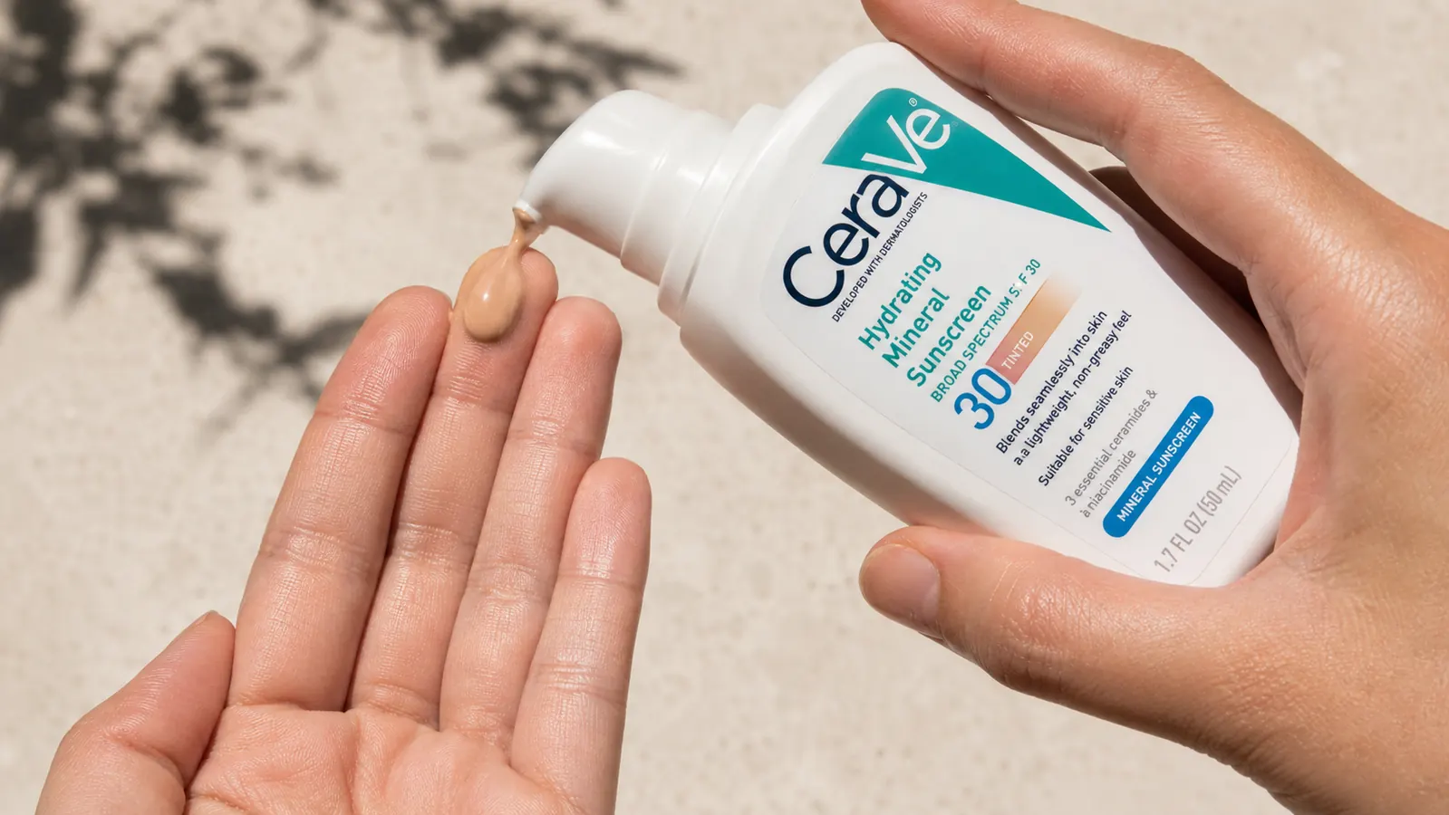 Hand dispensing a small amount of tinted mineral sunscreen onto fingertips