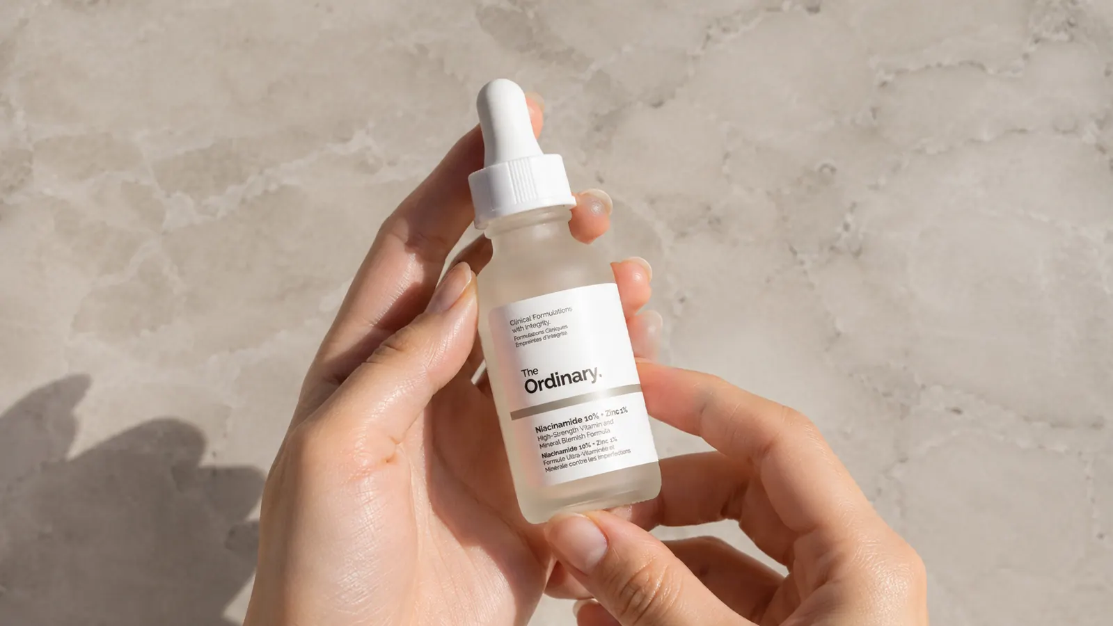A bottle of The Ordinary Niacinamide 10% plus Zinc 1% serum held in one hand against a light stone background