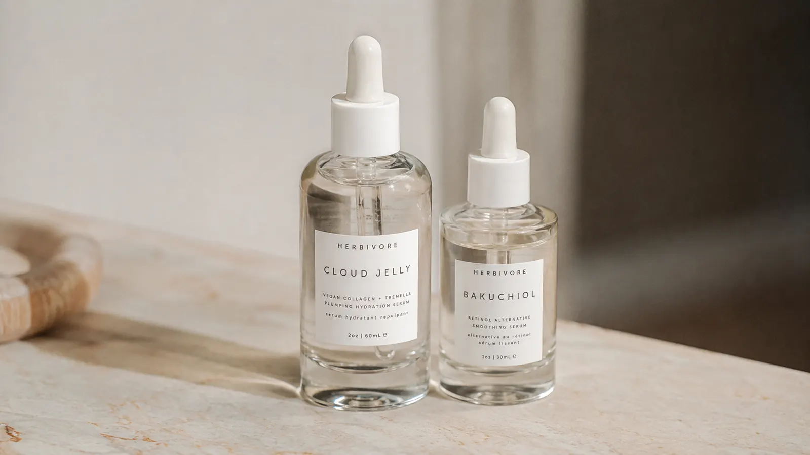 Two serum bottles side by side on a marble surface, one small and one larger, illustrating size options
