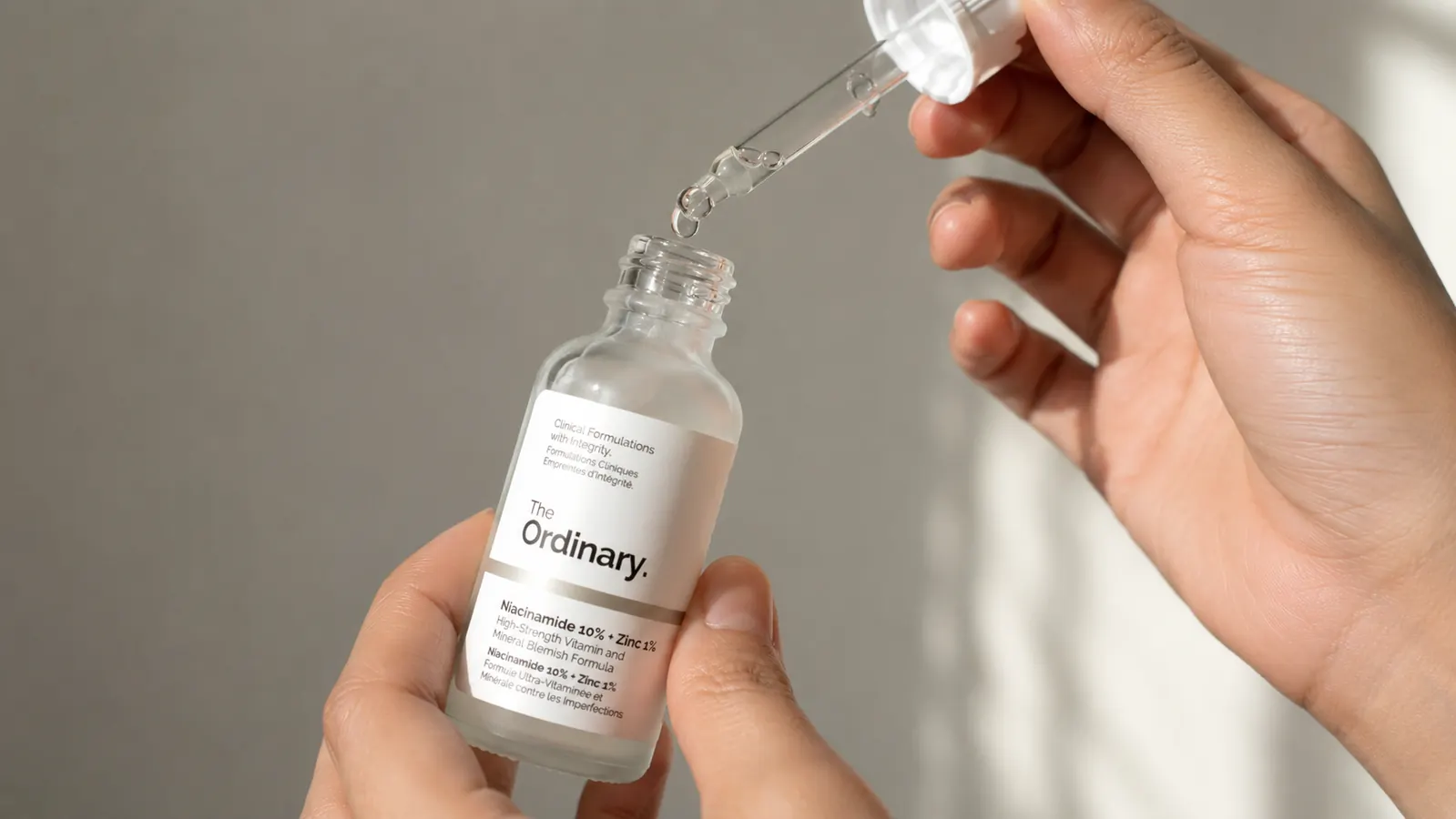 Hand holding The Ordinary Niacinamide 10% + Zinc 1% dropper bottle, close-up showing dropper tip