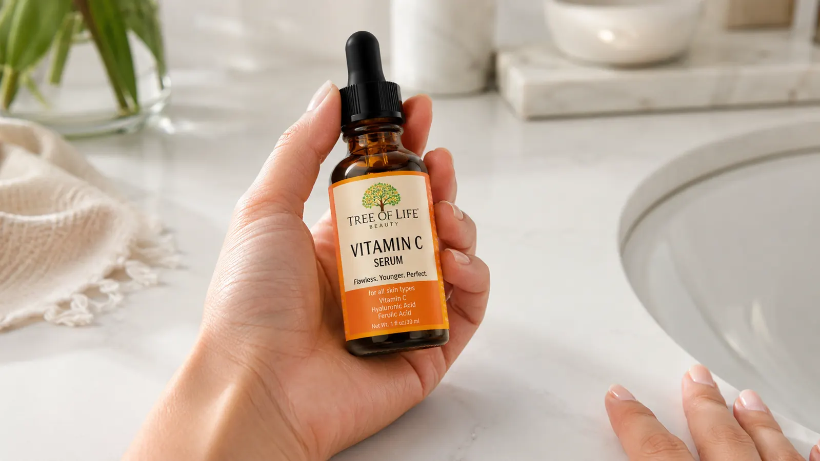 Tree of Life Vitamin C serum bottle held in an open palm over a white bathroom countertop